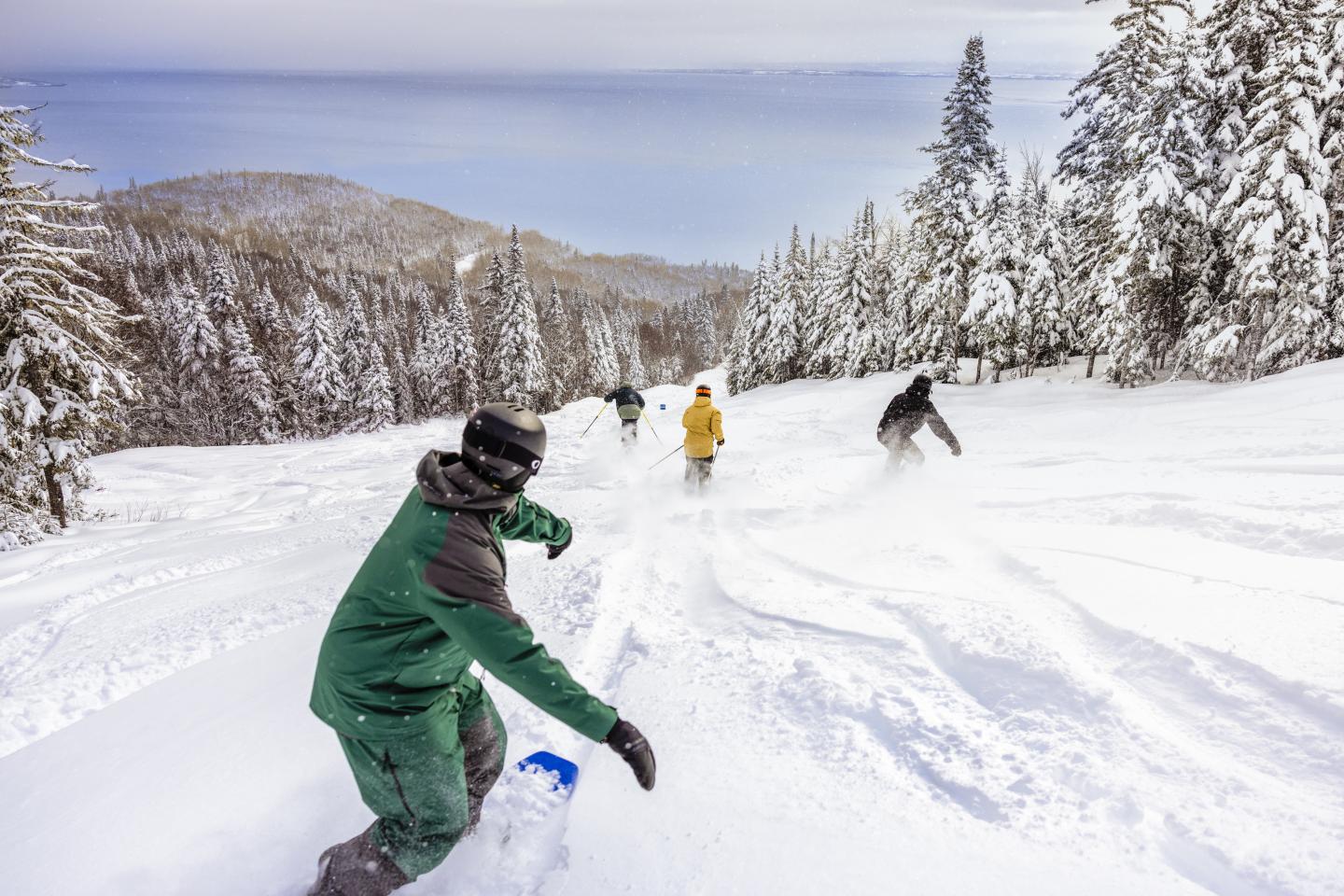 Snowboarders descendant une pente enneigée entourée d'arbres.